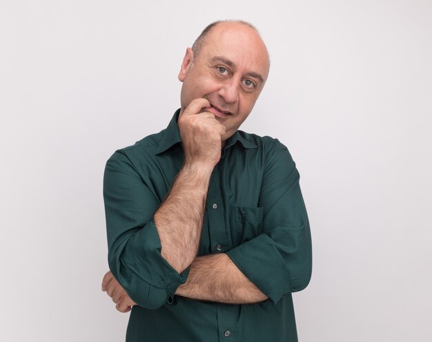 Impresionado hombre de mediana edad vestido con camiseta verde poniendo el dedo en la boca aislado en la pared blanca