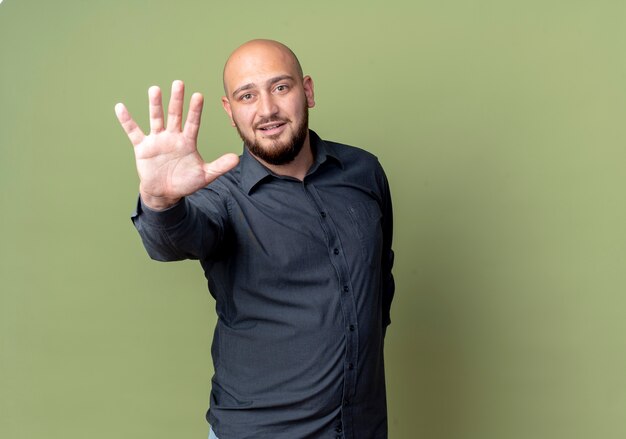 Impresionado joven calvo call center hombre estirando la mano mostrando cinco aislados en verde oliva con espacio de copia