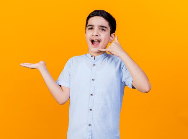 Impresionado joven caucásico haciendo gesto de llamada mirando a la cámara mostrando la mano vacía aislada sobre fondo naranja con espacio de copia