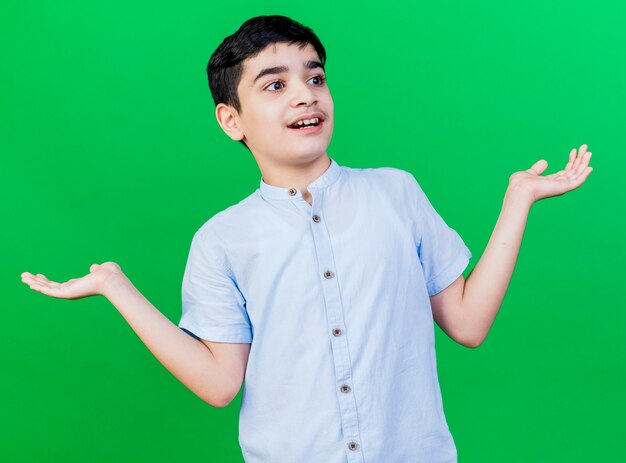 Impresionado joven caucásico mirando al lado mostrando las manos vacías aisladas en la pared verde