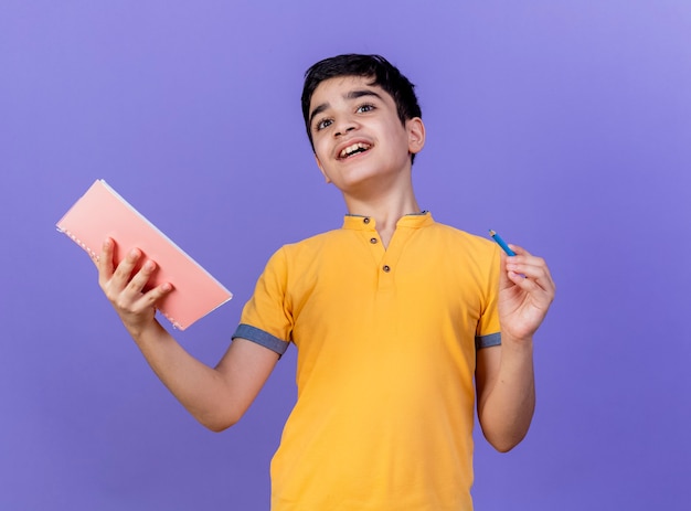 Foto gratuita impresionado joven caucásico sosteniendo bloc de notas y lápiz aislado en la pared púrpura