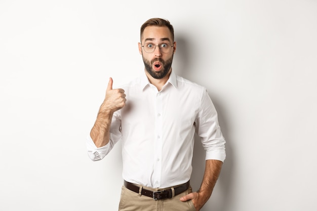 Impresionado joven empresario mostrando el pulgar hacia arriba, elogia algo bueno, me gusta y está de acuerdo, blanco