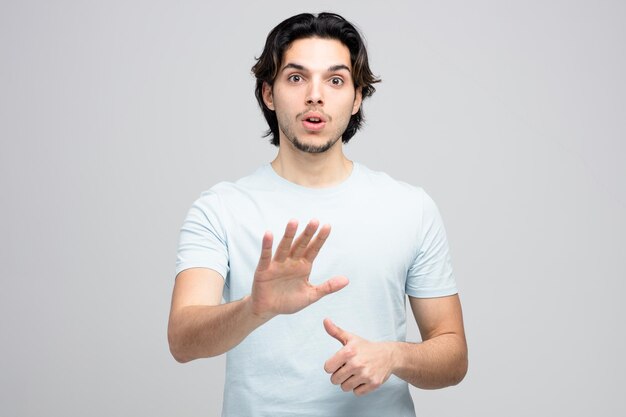 Impresionado joven guapo mirando a la cámara mostrando el pulgar hacia arriba y ningún gesto aislado sobre fondo blanco.