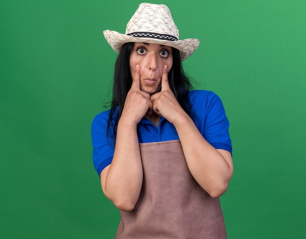 Foto gratuita impresionado joven jardinero caucásico mujer vestida con uniforme y sombrero tirando hacia abajo los párpados