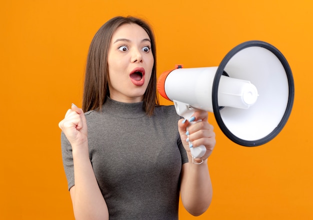 Foto gratuita impresionado joven mujer bonita apretando el puño mirando directamente y hablando por el altavoz