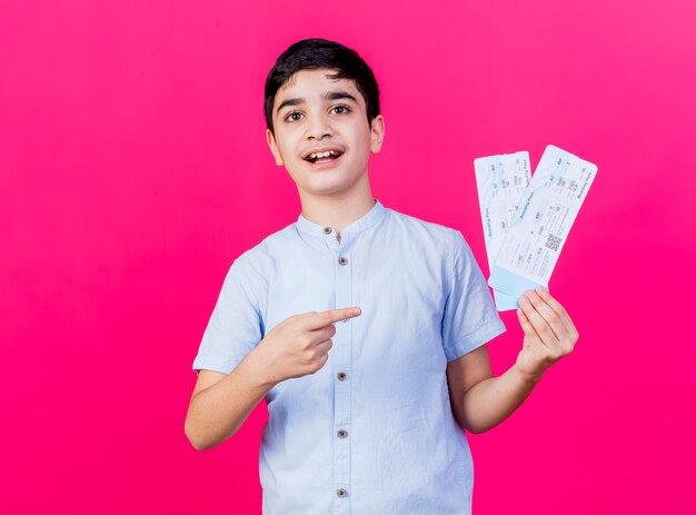 Impresionado joven sosteniendo y apuntando a los billetes de avión mirando al frente aislado en la pared rosa