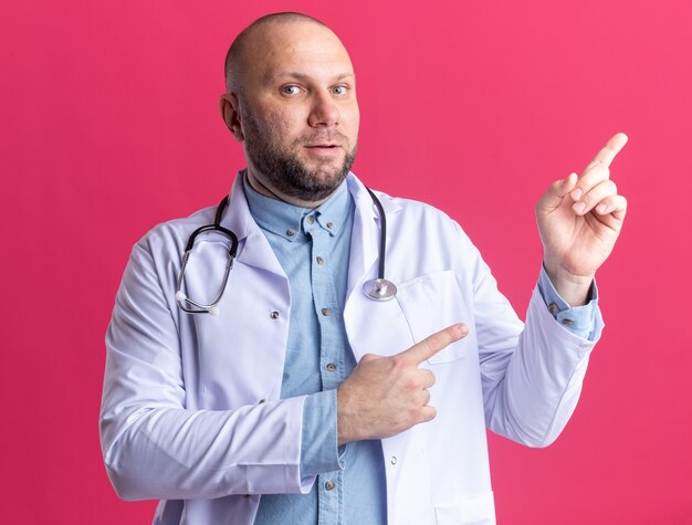 Impresionado médico varón de mediana edad vistiendo bata médica y estetoscopio apuntando hacia arriba