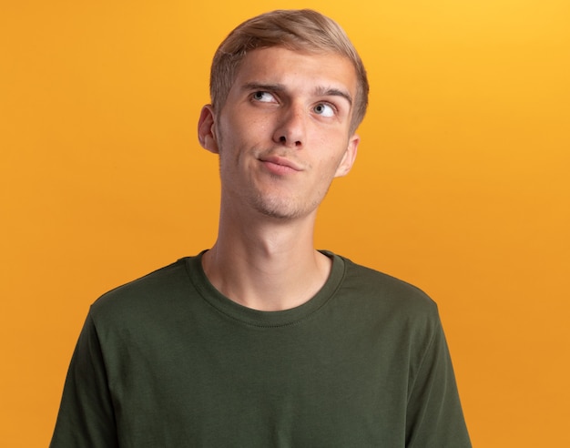 Impresionado mirando al lado chico guapo joven con camisa verde aislado en la pared amarilla