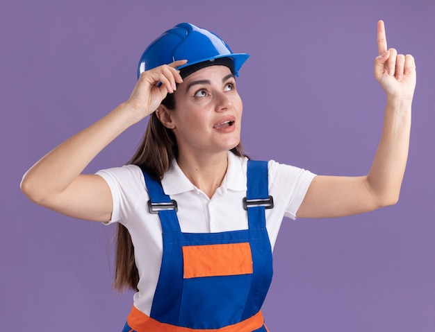 Impresionado mirando a la mujer joven constructora en puntos uniformes en aislados en la pared púrpura