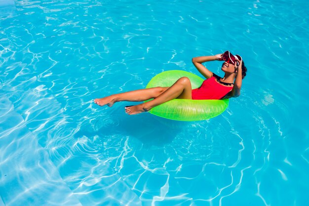 Impresionante bronceada hermosa joven en bikini nadando en la piscina y relajarse en elegantes trajes de baño.