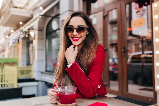 Impresionante chica caucásica en chaqueta roja sonriendo en café