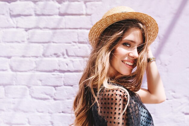 Impresionante dama de pelo largo con ojos grandes posando afuera caminando por la pared de ladrillo