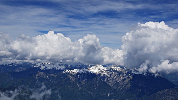 Impresionante disparo de alto ángulo de montañas nevadas bajo las nubes y el cielo de fondo