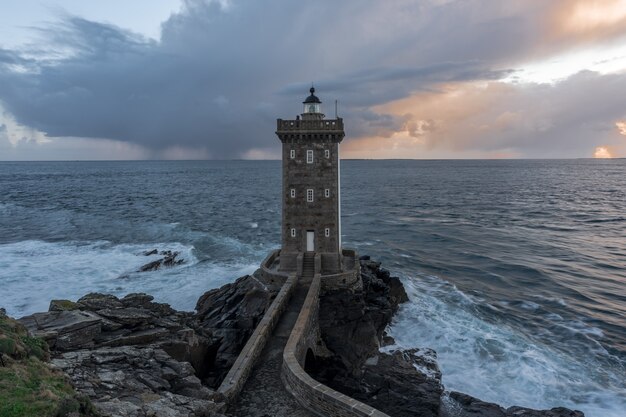 Impresionante foto de un hermoso faro de pie a la orilla del mar bajo el cielo nublado