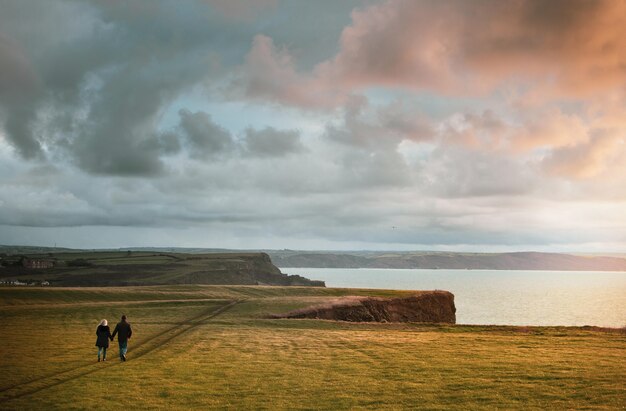 Impresionante foto de una pareja caminando tomados de la mano en un acantilado al atardecer