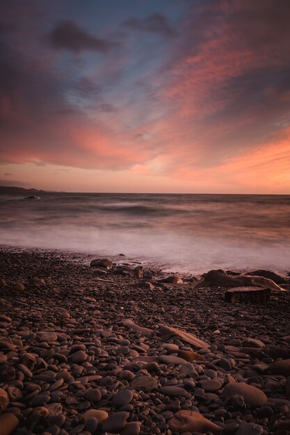 Impresionante foto de una playa rocosa sobre un fondo de puesta de sol