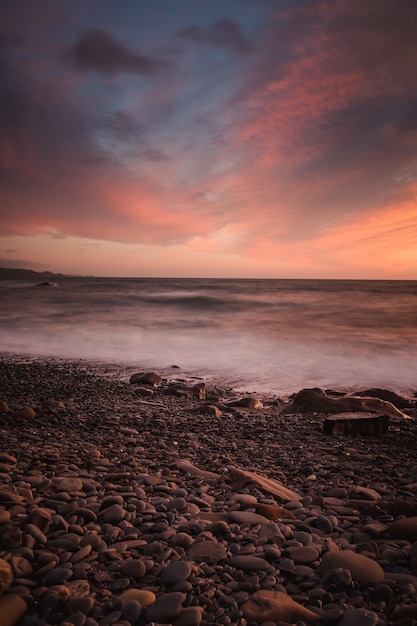 Impresionante foto de una playa rocosa sobre un fondo de puesta de sol