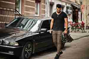 Foto gratuita impresionante hermoso hombre macho alto de barba árabe con gafas y camiseta negra caminando contra un coche de negocios