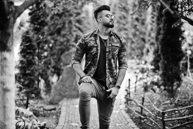 Impresionante hermoso hombre macho macho de barba árabe alto con gafas y chaqueta militar posado al aire libre