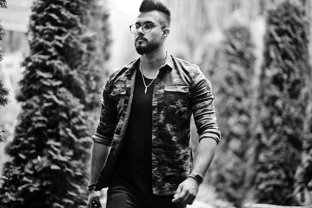 Impresionante hermoso hombre macho macho de barba árabe alto con gafas y chaqueta militar posado al aire libre