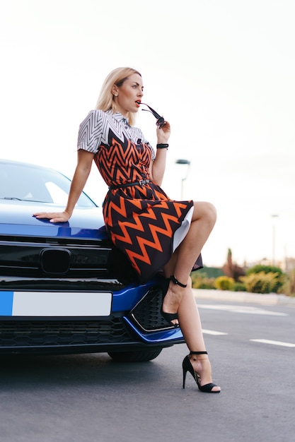 Impresionante joven vestido waring posando delante de su coche al aire libre, conductor de propiedad