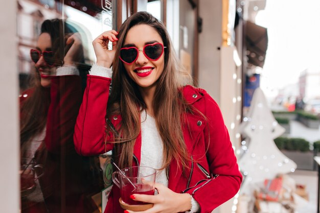 Impresionante mujer blanca con maquillaje de moda y manicura bebiendo té al aire libre