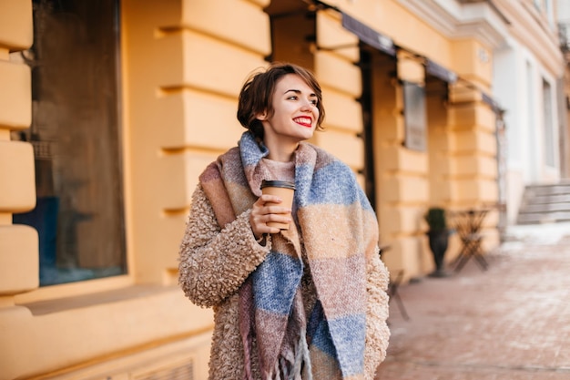 Impresionante mujer con bufanda larga bebiendo café Toma al aire libre de una chica elegante disfrutando de un día frío