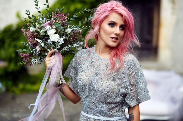 Impresionante mujer con cabello rosado se encuentra con gran ramo de boda