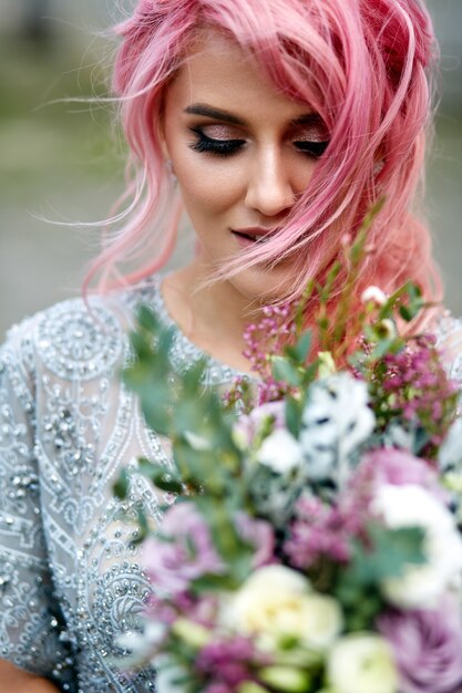 Impresionante mujer con cabello rosado se encuentra con gran ramo de boda