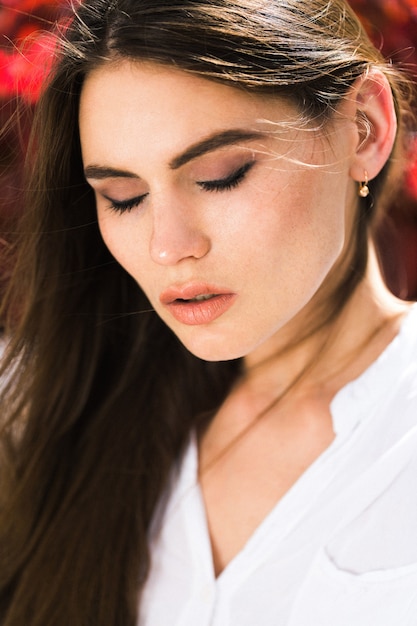 Impresionante mujer de ojos verdes se sienta ante las flores rojas