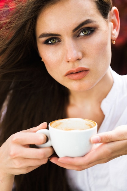 Impresionante mujer de ojos verdes se sienta ante las flores rojas