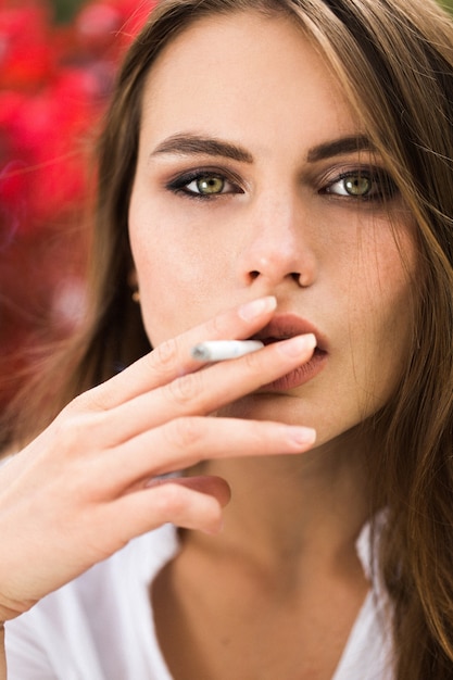 Impresionante mujer de ojos verdes se sienta ante las flores rojas