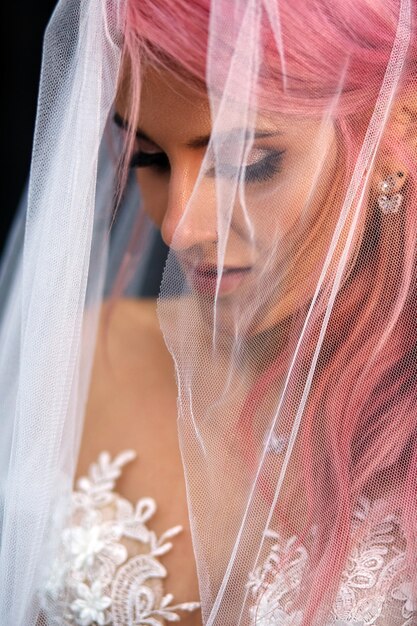 Impresionante novia con cabello rosado cubierto con velo ligero