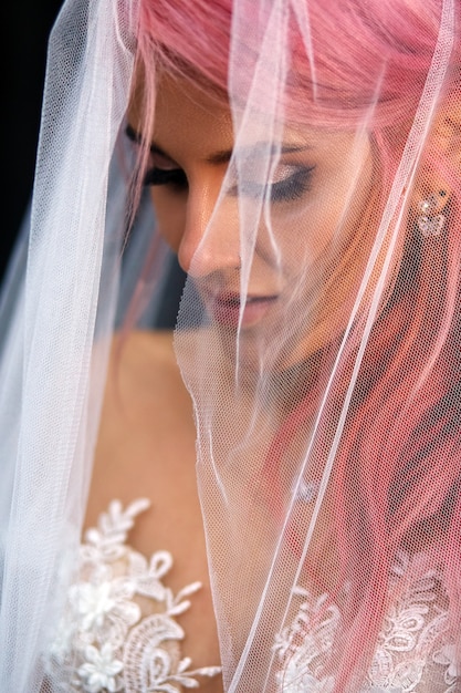 Impresionante novia con cabello rosado cubierto con velo ligero