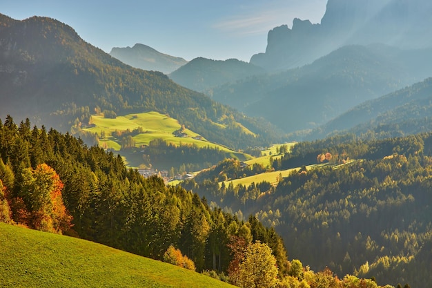 Impresionante paisaje otoñal en el pueblo de Santa Maddalena con árboles coloridos de la iglesia y prados bajo los rayos del sol naciente Alpes Dolomitas Italia