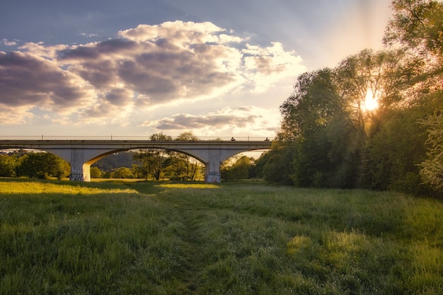 Impresionante puesta de sol sobre un bosque verde con un largo puente en el medio