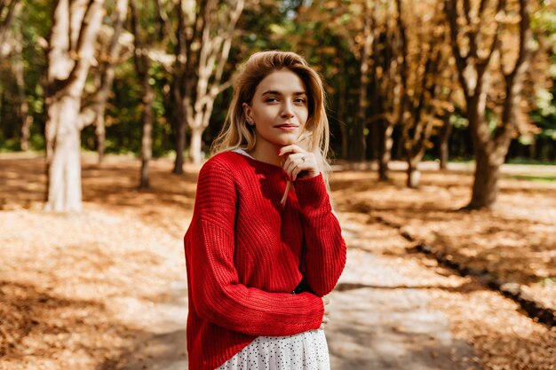 Impresionante rubia con ropa elegante mirando lejos en el bosque de otoño.