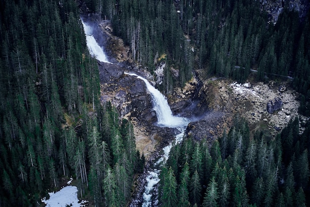 Impresionante toma de alto ángulo de una cascada en una roca rodeada por un bosque de abetos altos
