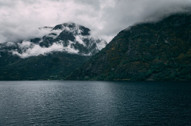 Impresionante toma de un lago rodeado de montañas nevadas bajo el cielo brumoso en Noruega