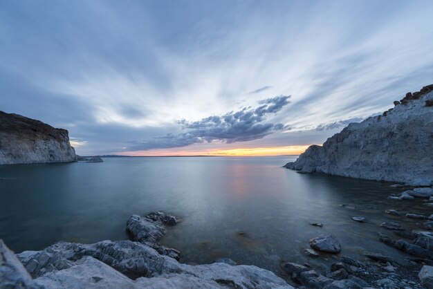 Impresionante toma del océano con colinas nevadas a los lados y una hermosa puesta de sol.