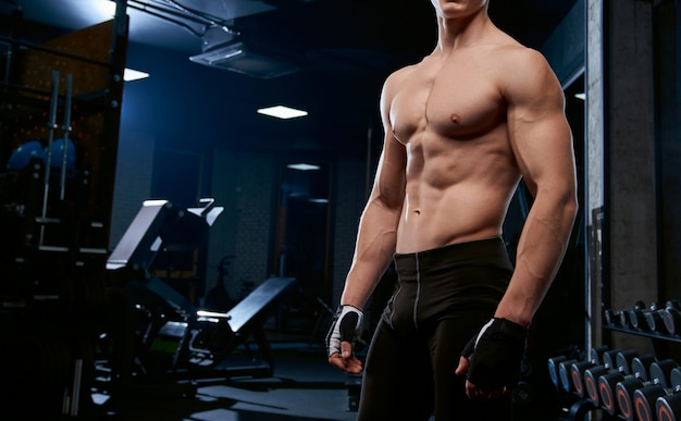 De incógnito deportista sin camisa posando en el gimnasio.