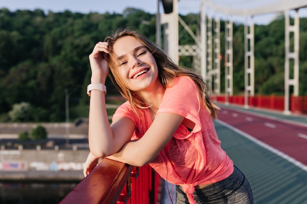 Increíble chica morena riendo después del entrenamiento. Tiro al aire libre de feliz dama blanca pasando la mañana en el estadio.