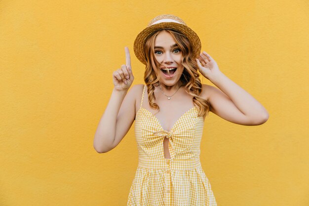 Increíble chica posando con sonrisa de sorpresa. Mujer joven alegre que expresa emociones positivas mientras posa en vestido amarillo.