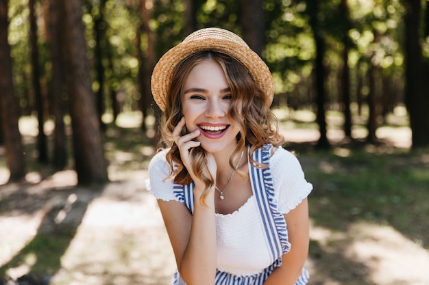 Foto gratuita increíble chica rizada con sombrero de paja, pasar tiempo en el bosque. foto al aire libre de una hermosa mujer sonriente posando en la naturaleza.