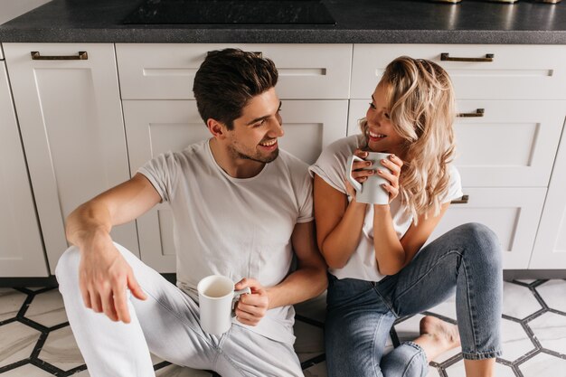 Increíble chica rubia pasando la mañana con su novio. Atractiva mujer caucásica tomando café con su marido.