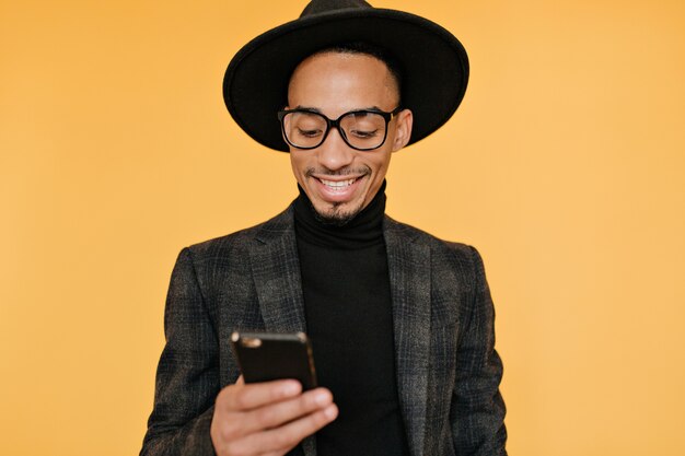 Increíble chico africano barbudo enviando mensajes de texto message.glad mulato modelo masculino mirando su teléfono con una sonrisa.