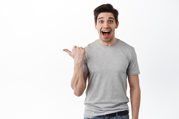 Foto gratuita increible. chico feliz emocionado sonriendo, apuntando a un lado en el espacio de la copia, mostrando una oferta de promoción impresionante y regocijo, de pie sobre fondo blanco.