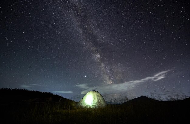 Increíble cielo estrellado en las montañas y carpa iluminada en el campamento