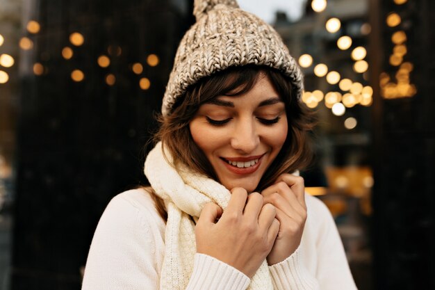 Increíble dama encantadora con sombrero blanco tejido y suéter tejido sonriendo