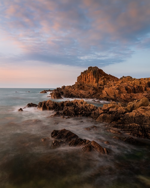 Increíble foto de una playa rocosa cerca de Fort Houmeton un fondo de puesta de sol en Guernsey